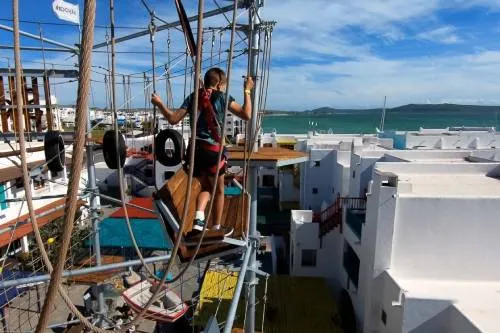 Iia boy walks among the ropes as a guide on the sky park in langebaan as the view is over the buildings of club mykonos and the langebaan lagoon in a distance.